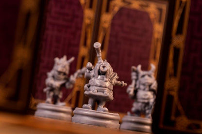 Three unpainted grey fantasy miniatures, with a cyclops-like figure in focus at the center.