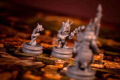 Two gray goblin board game miniatures on a game map, one holding a staff. A third is blurred.