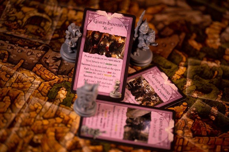 Pink "Goblin Infantry" cards and gray fantasy miniatures set on a detailed, stone-patterned board game map.