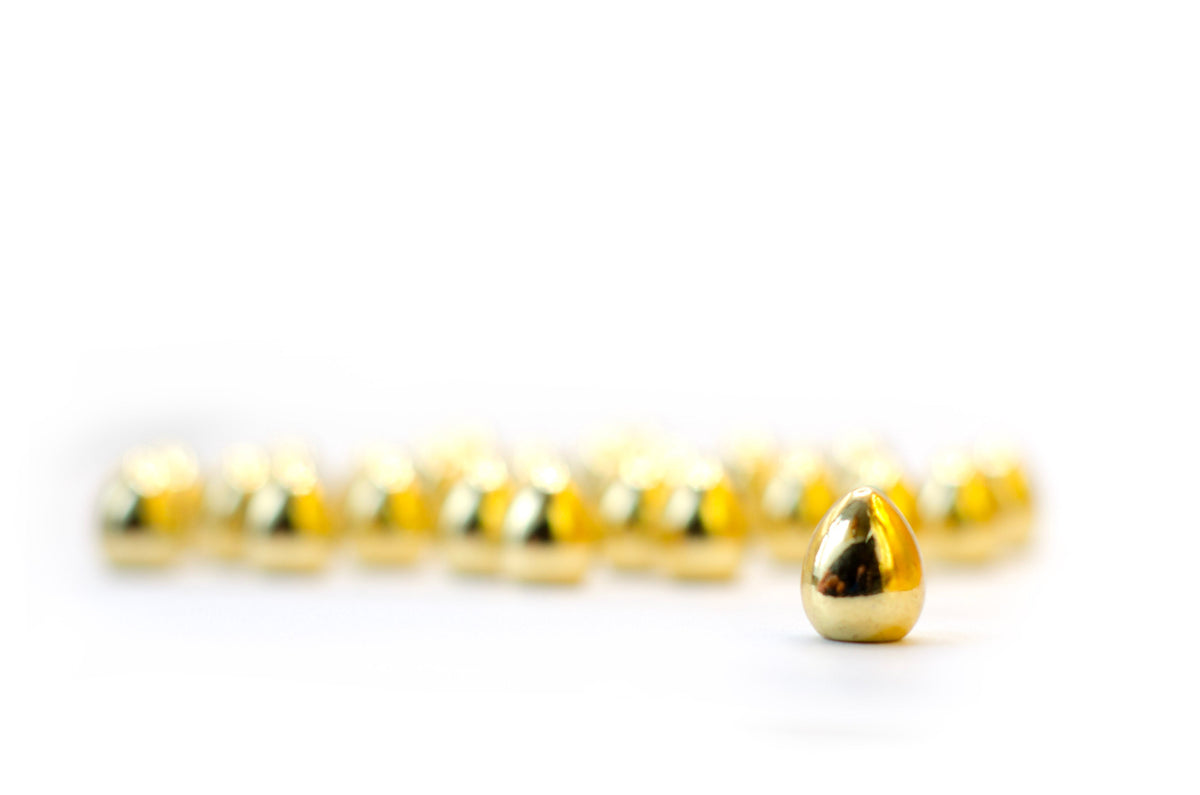 Focused golden egg stands before a blurred line of gold eggs on a white surface
