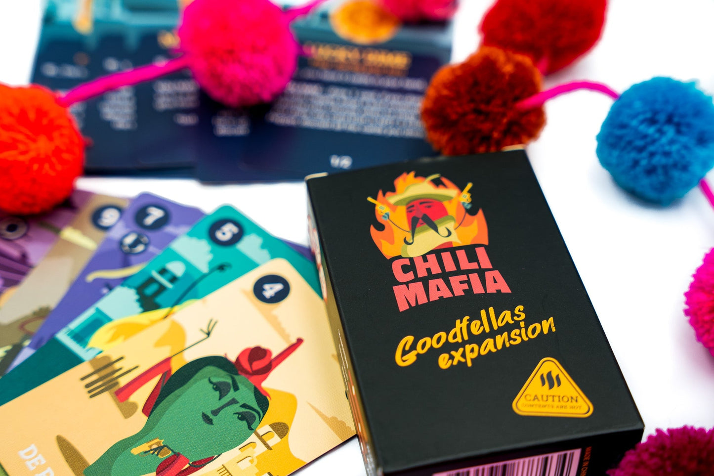 Chili Mafia Goodfellas Expansion card game box and scattered playing cards featuring colorful illustrations and numerical values