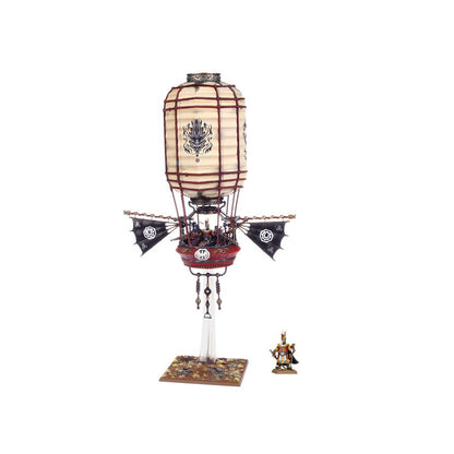 An ornate fantasy airship model, shaped like a lantern with black bat-wings and a red gondola, next to a warrior figure