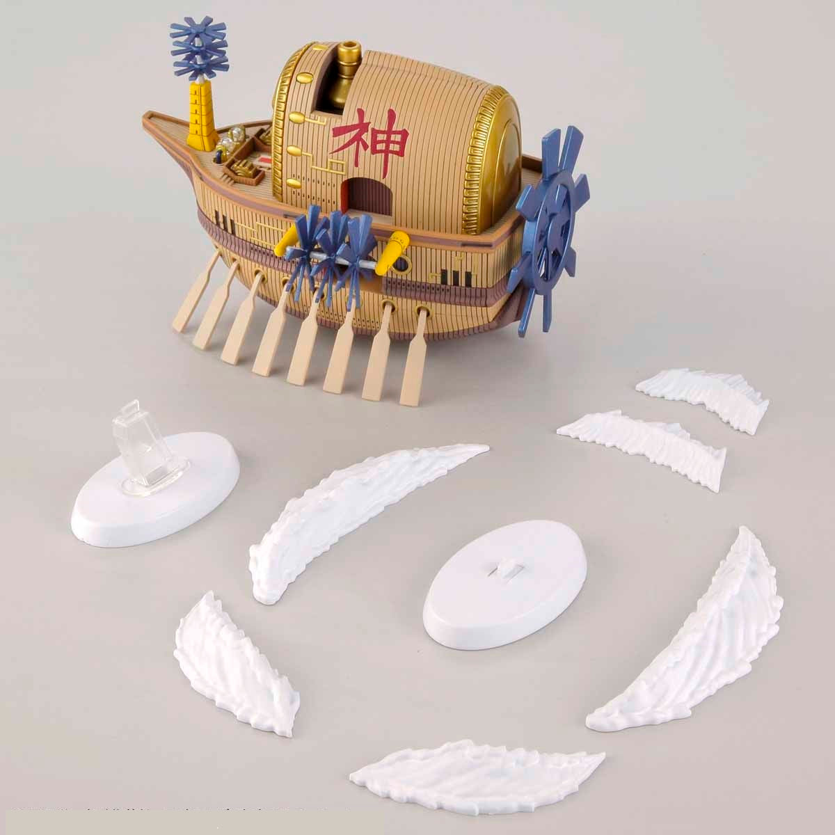 A model ship with a golden face on the bow, blue paddle wheels, oars, and the character 'ç¥ž' on its side, with white cloud effects