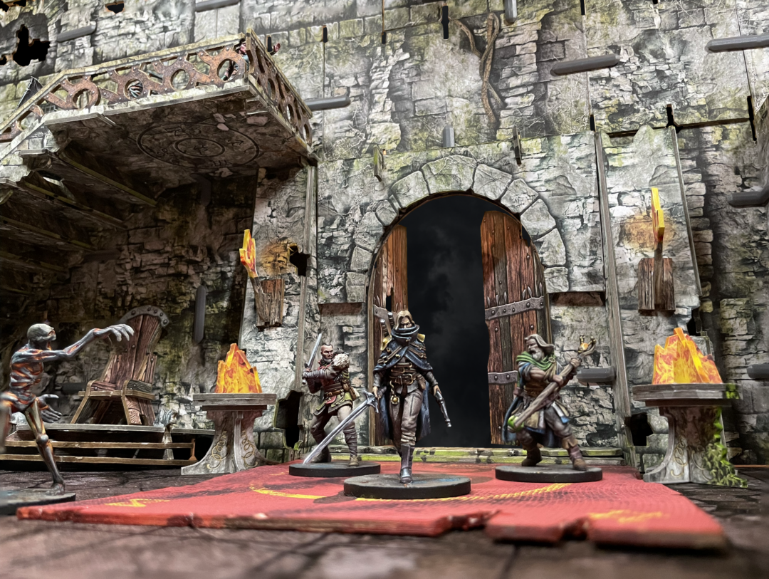 A fantasy tabletop game scene with three miniature heroes on a red rug facing a zombie in a stone dungeon with a door and balcony