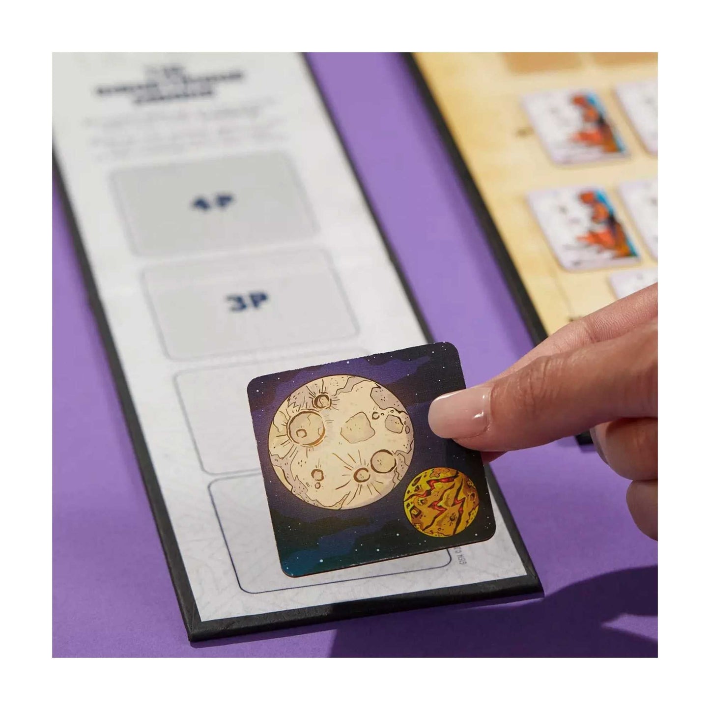 Hand placing a space-themed game token (moon and planet) onto a game board slot