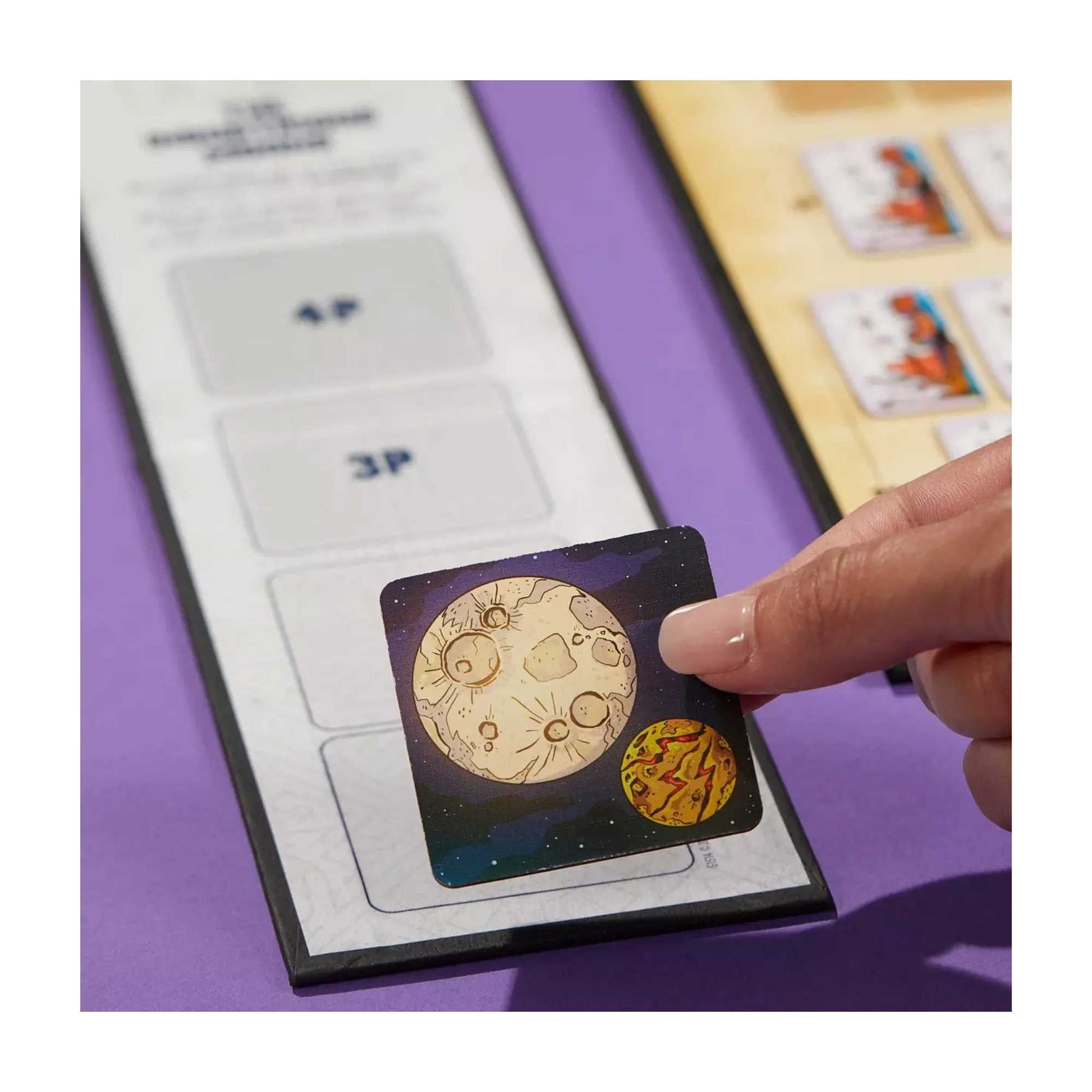 Hand placing a space-themed game token (moon and planet) onto a game board slot