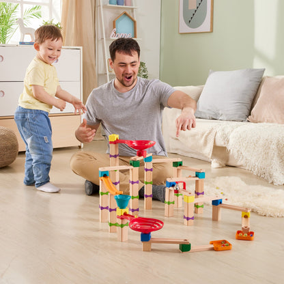 Smiling father and toddler playing with a colorful wooden marble run toy on the floor