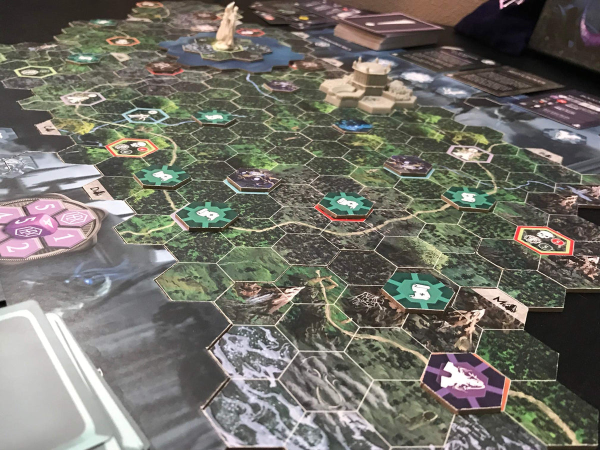 A fantasy-themed board game laid out on a table. It features hexagonal tiles, numerous tokens, a castle, a statue, and stacks of game cards