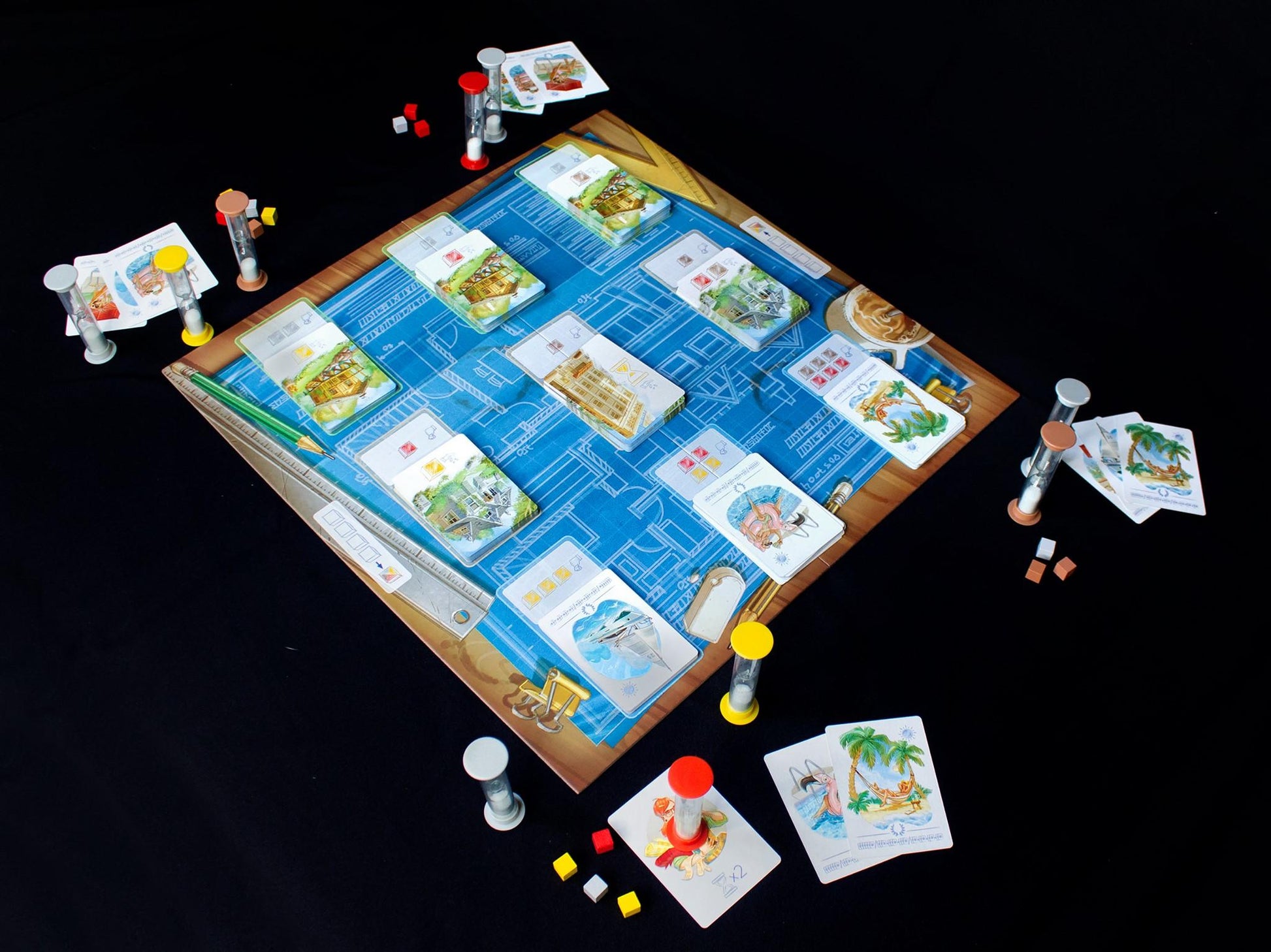A strategic board game set with blueprints timer hourglasses and illustrated cards featuring buildings and scenes scattered on a black surface