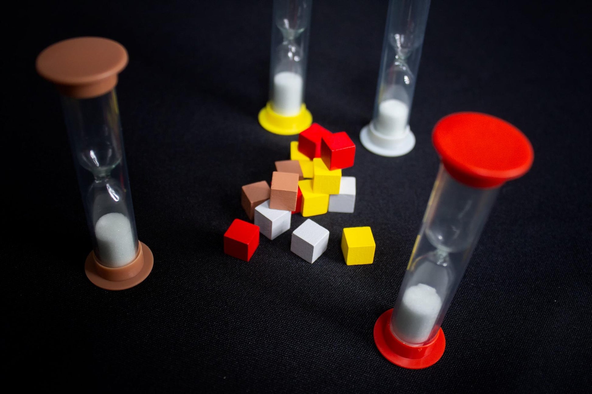 Four hourglasses of various sizes and colors with wooden blocks of various colors scattered around