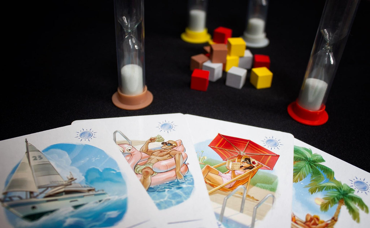 Board game components including hourglass timers colored cubes and cards with tropical illustrations