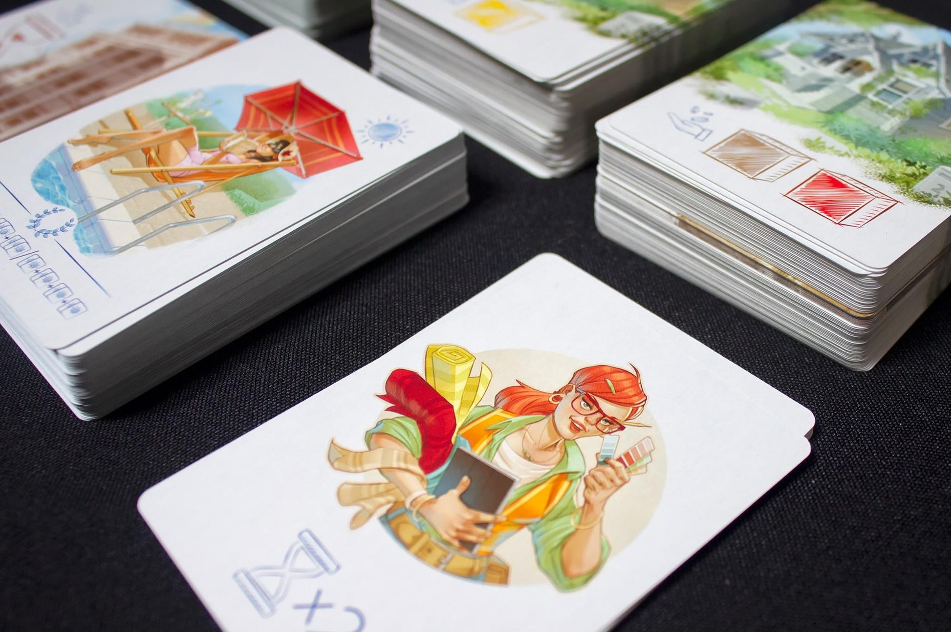 Stacks of colorful game cards featuring illustrations of relaxing scenes and architectural sketches