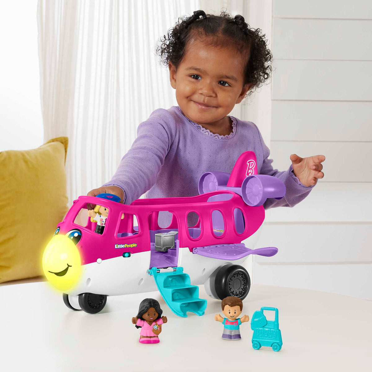 Smiling toddler plays with a pink and white Little People airplane, with small figures around it