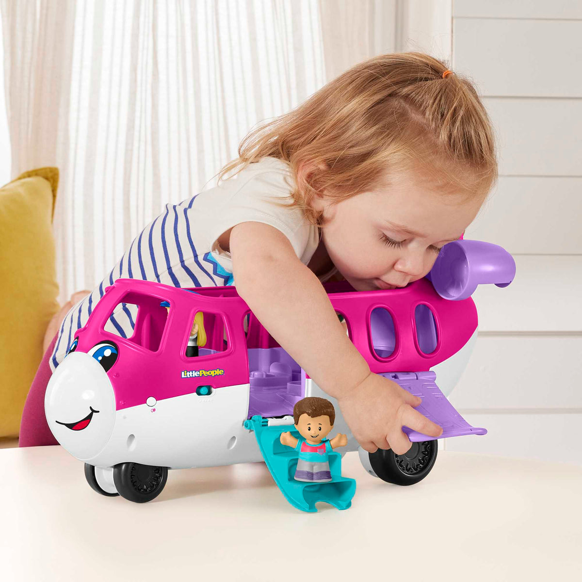 Toddler intently plays with a colourful Little People airplane toy on a table, manipulating a figure