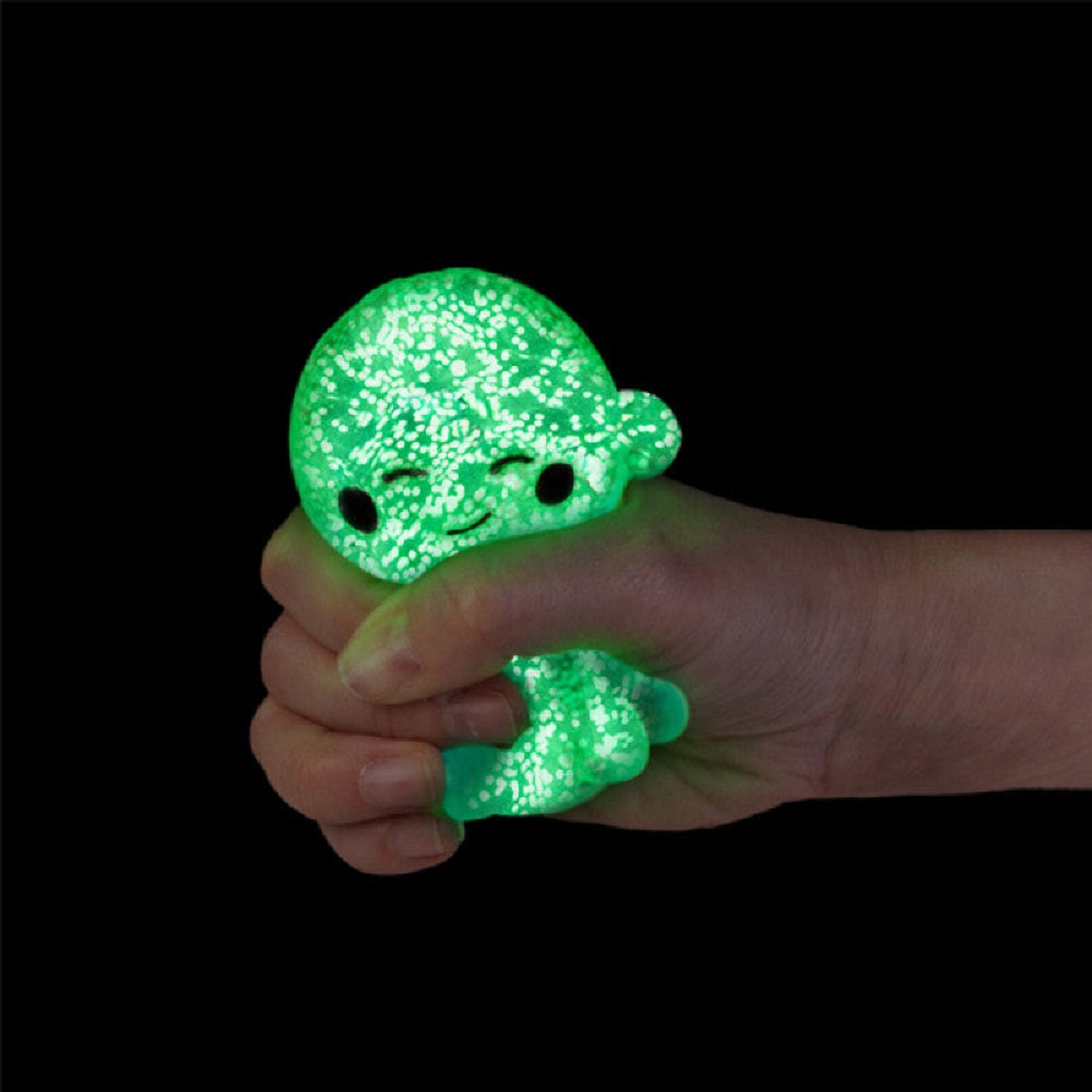 Hand squeezes a glowing green stress toy with a smiley face in the dark