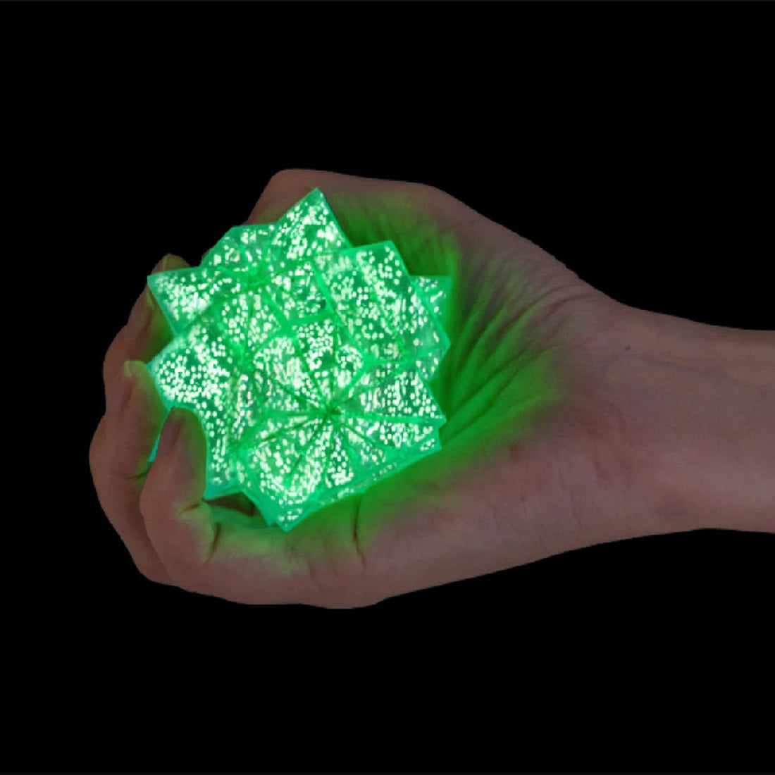 Hand gripping a luminous, green star-shaped sensory toy on a dark background