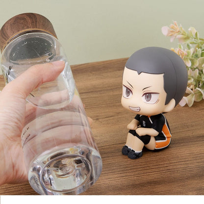 Hand holding a clear water bottle with a wood cap, next to a small, sitting chibi anime figure in a black jersey