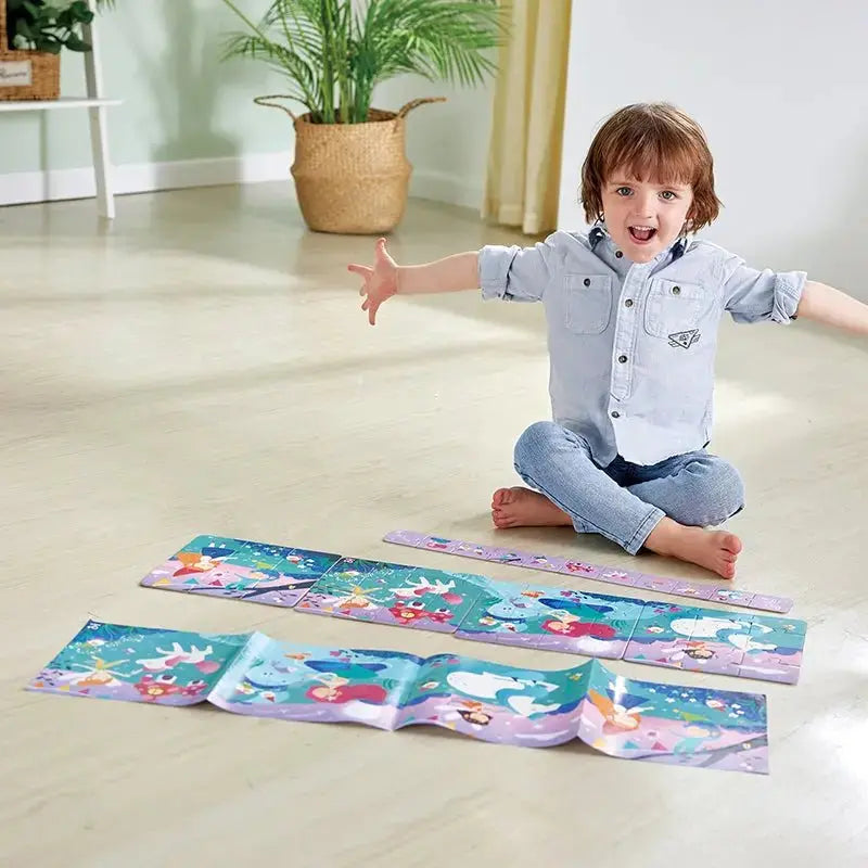 An excited boy sits on the floor with arms wide, playing with long, colourful story puzzles.
