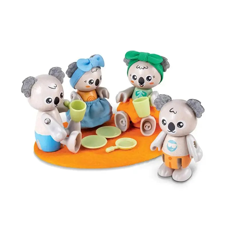 Four koala toys, three seated and one standing, having a tea party with cups and plates on an orange mat.