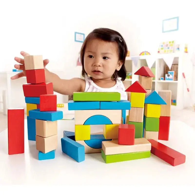 A young child stacks colourful wooden building blocks on a white table, creating various structures.