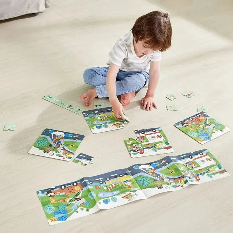 A boy sits on the floor, connecting pieces of a long, colourful street scene puzzle with vehicles.