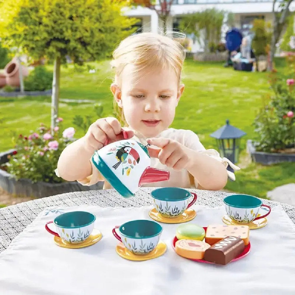 Child pouring from a toucan toy teapot into a cup during a garden tea party