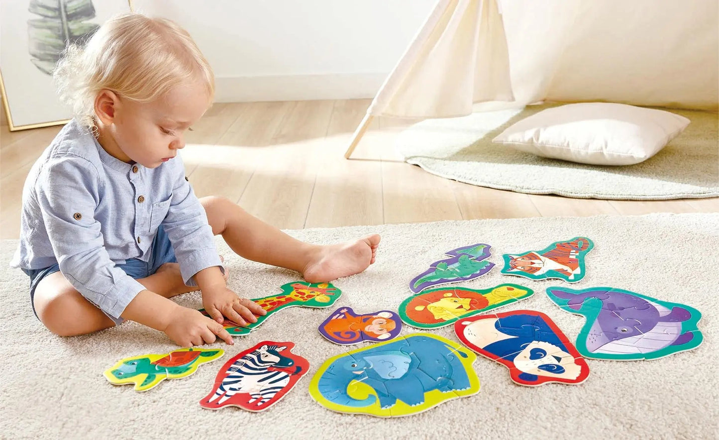 A blond toddler sits on a rug, playing with colourful animal-shaped puzzles.