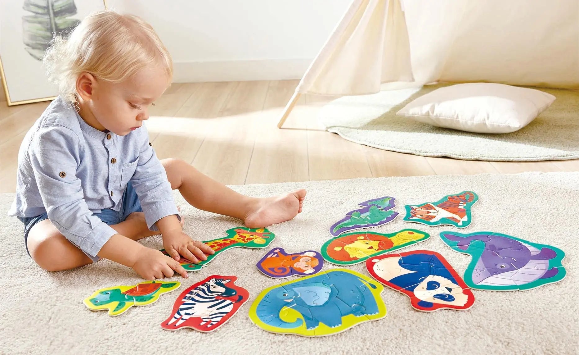 A blond toddler sits on a rug, playing with colourful animal-shaped puzzles.
