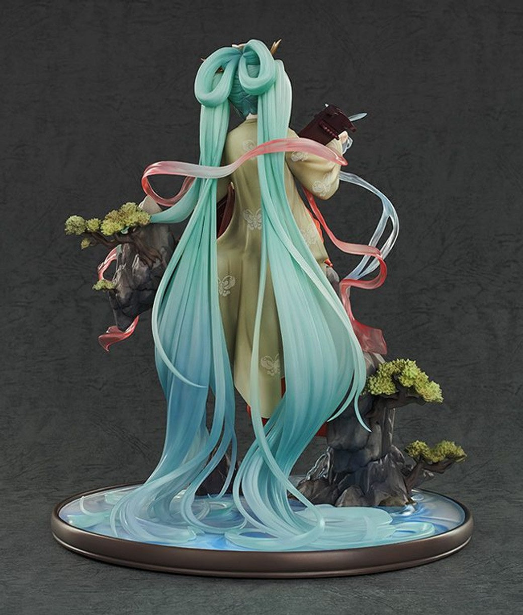 A Hatsune Miku Gao Shan Liu Shui version figure viewed from the back, featuring long teal hair flowing over a light traditional dress on a water base with rocks and trees