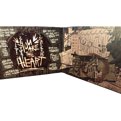 Distressed book spread: "YOU ARE THE HEART" on dark wood (left), surrounded by text; chaotic papers & diagrams (right)
