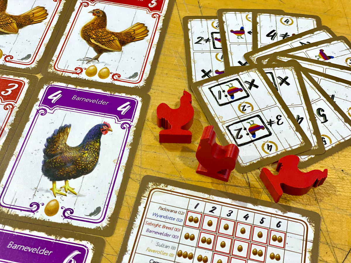 Board game components: cards with chicken illustrations, red chicken meeples, and a score sheet on a wooden table.