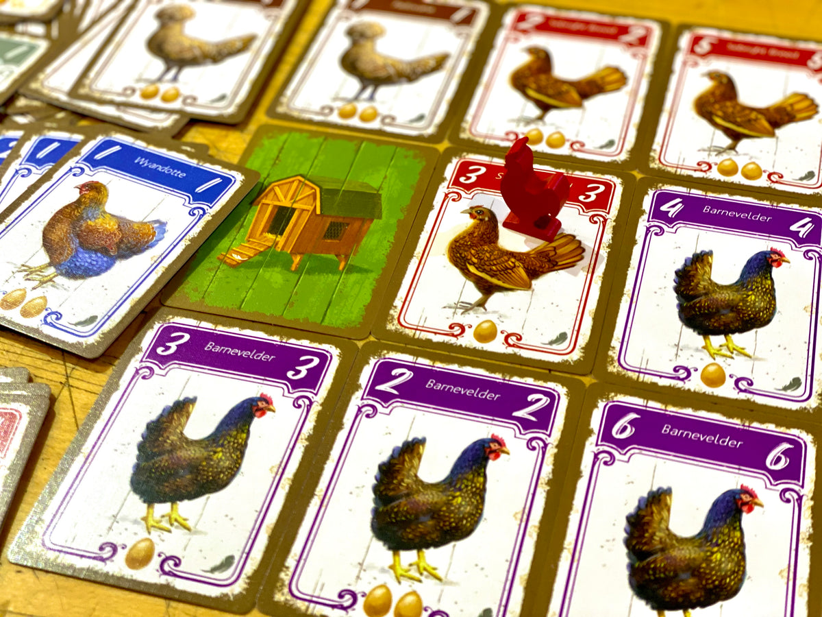 Close-up of a board game with chicken cards, eggs, a red chicken token, and a chicken coop tile.