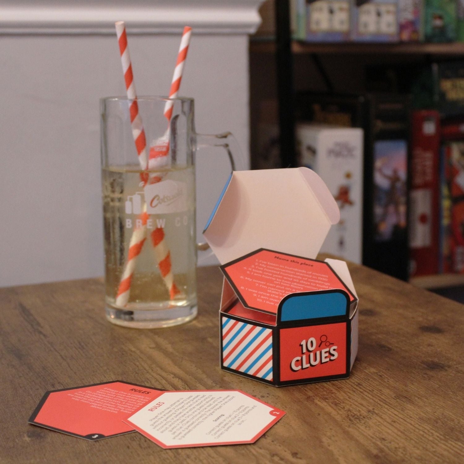 Open "10 Clues" game box, cards, and a drink with striped straws on a wooden table