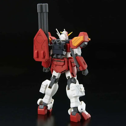 A red and white Gundam model stands with a large shoulder cannon and a shield, facing slightly away