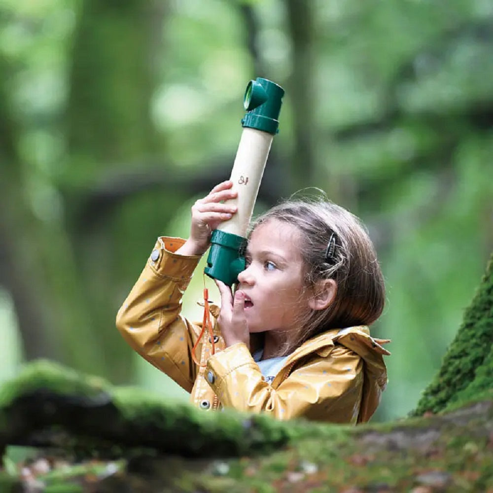 Young girl in a yellow jacket looking through a green and wood nature viewer in a forest