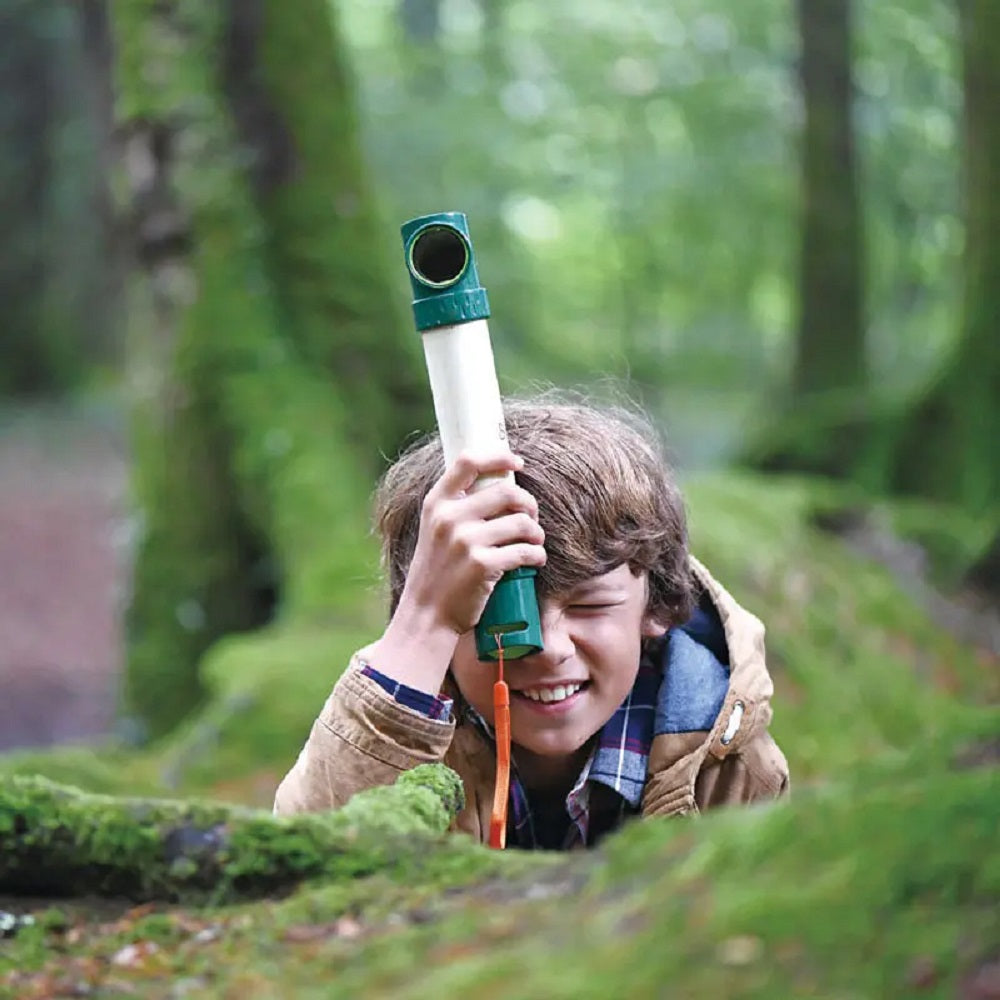 Smiling boy using a scope to look at the ground in a mossy forest