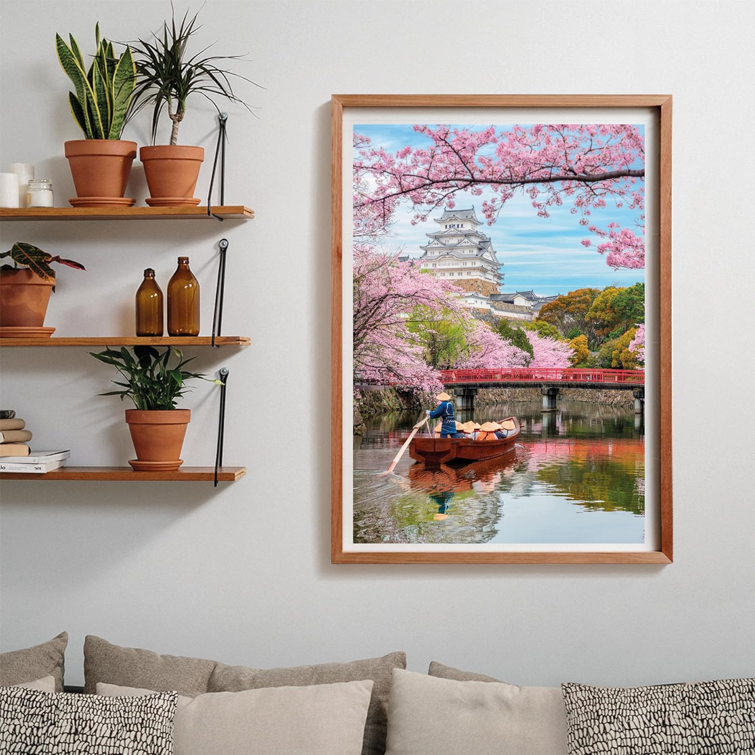 A person rows a boat on a moat beneath a white Japanese castle and red bridge, framed by pink cherry blossoms.