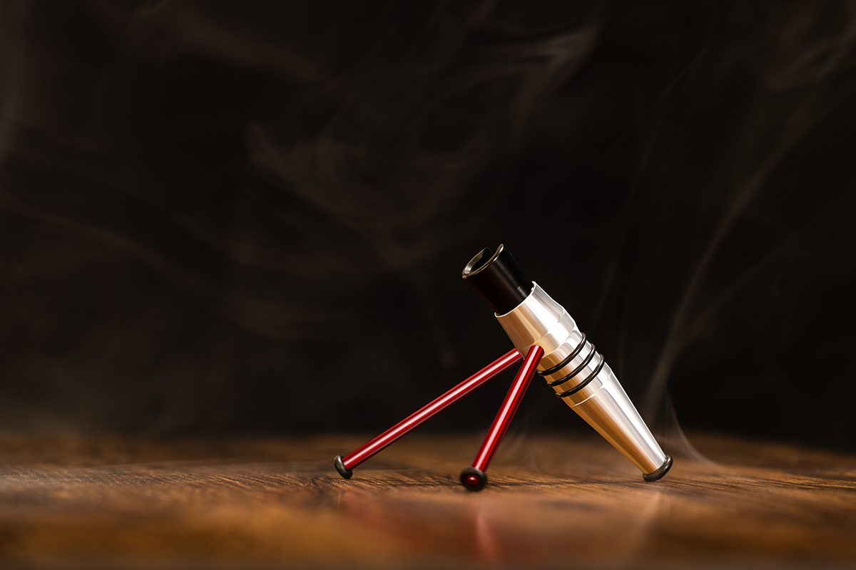 The Harder & Steenbeck Airbrushes Display Stand, silver with red legs, rests on a wooden table with swirling smoke behind it