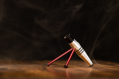 The Harder & Steenbeck Airbrushes Display Stand, silver with red legs, rests on a wooden table with swirling smoke behind it