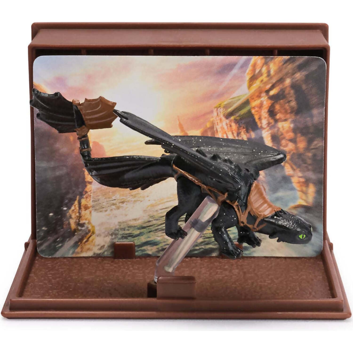 Black Toothless dragon figure with a brown prosthetic tail fin, standing in a brown display case, a scenic background of sunset cliffs and ocean is behind it