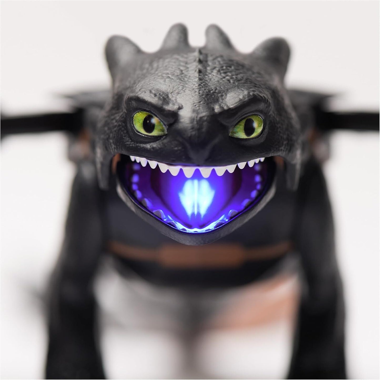 Close-up of black dragon toy with vivid green eyes, open mouth revealing sharp white teeth and a bright blue glow