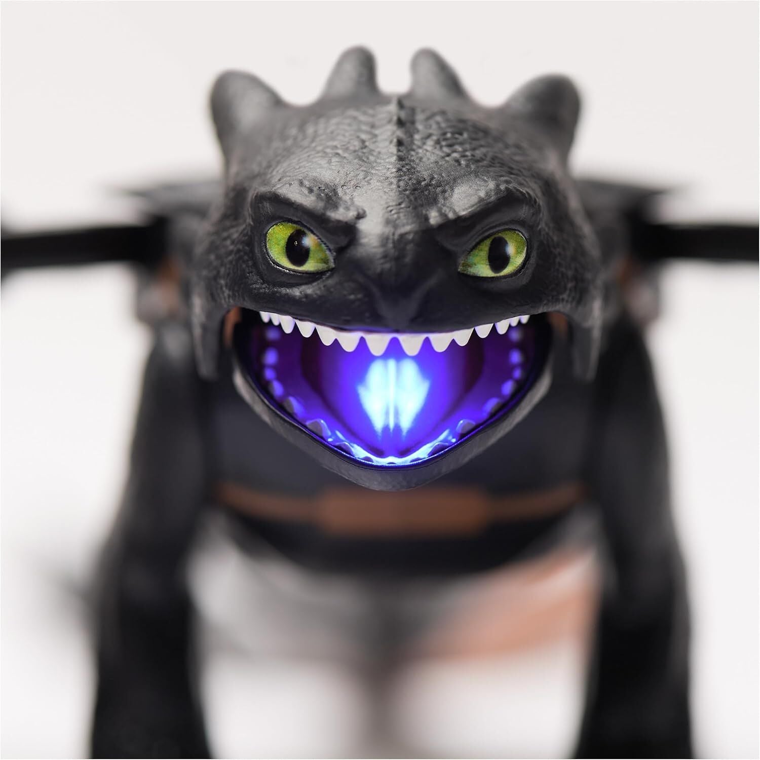 Close-up of black dragon toy with vivid green eyes, open mouth revealing sharp white teeth and a bright blue glow