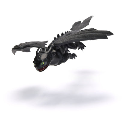 Black Toothless Night Fury dragon toy flying with green eyes, open mouth, and spread wings, casting a shadow