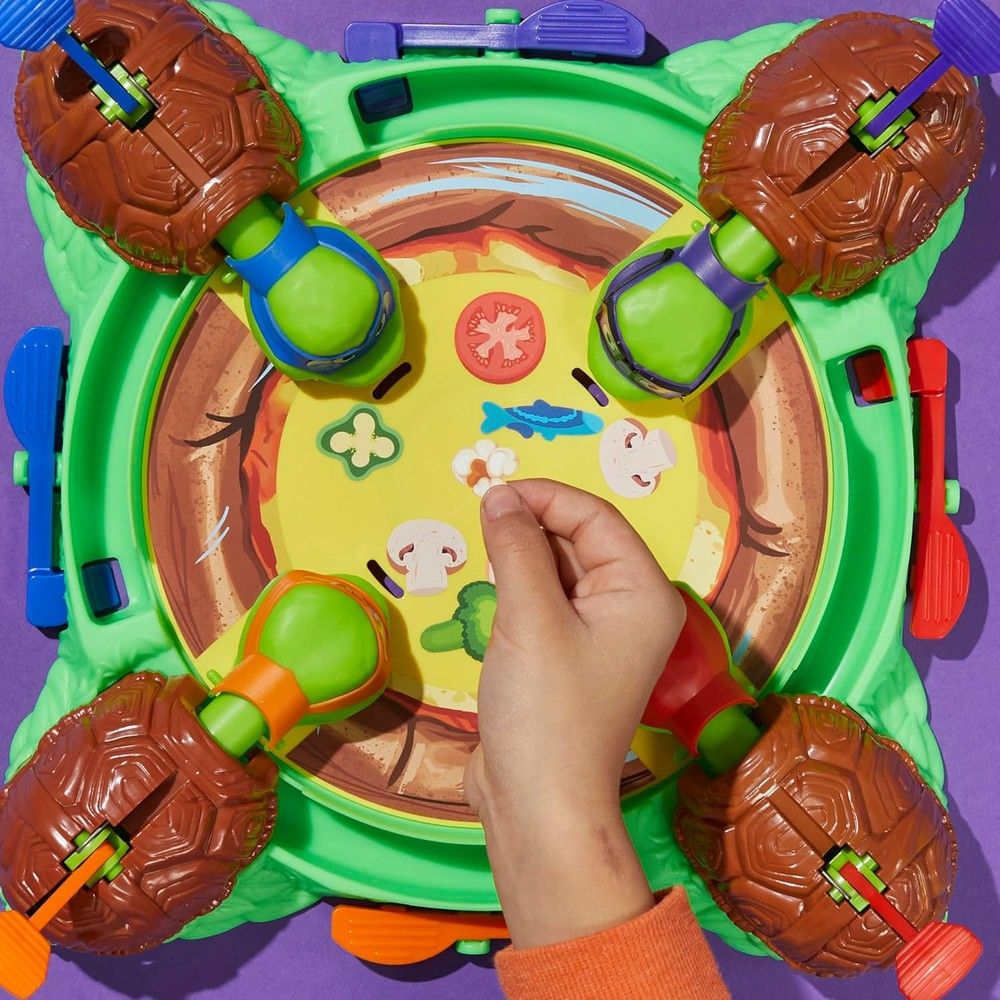 A child's hand plays a TMNT pizza board game, flicking turtle shell flippers to launch toppings
