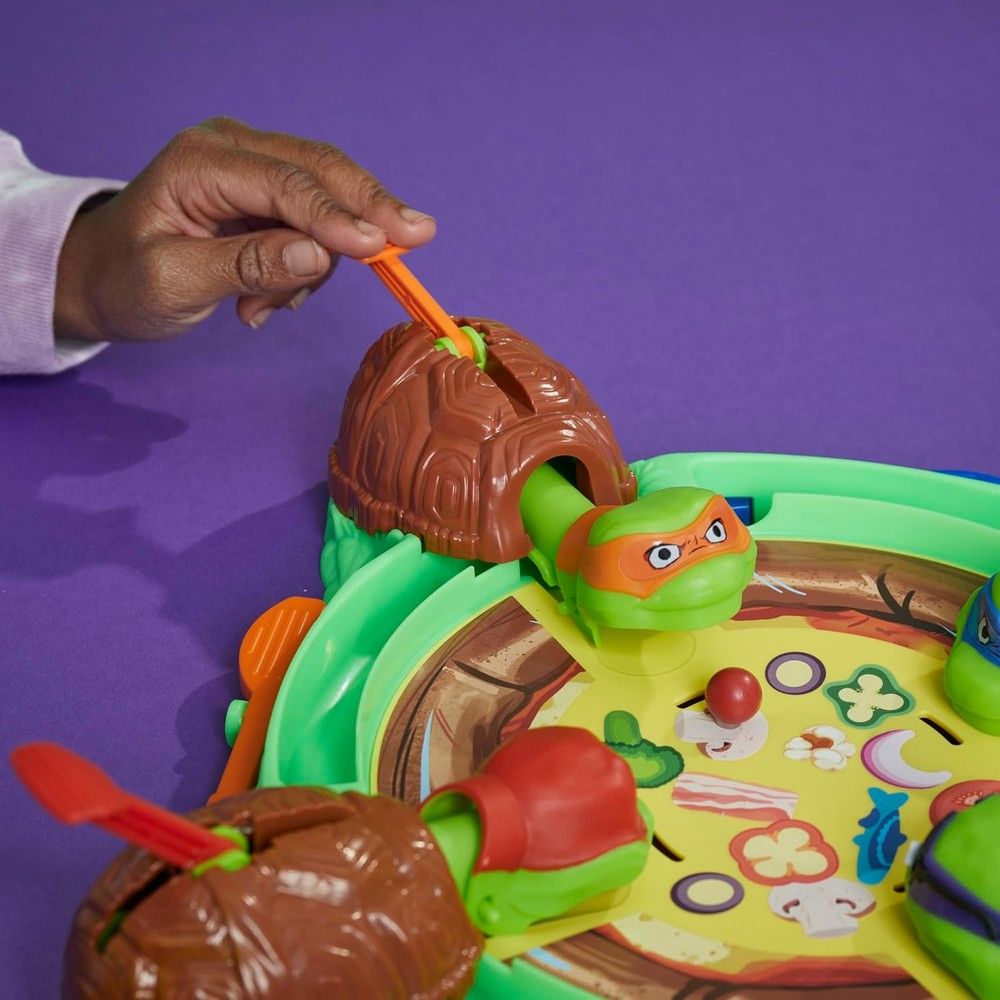 Hand pushes lever on a TMNT pizza game featuring green turtles with colorful masks and pizza toppings