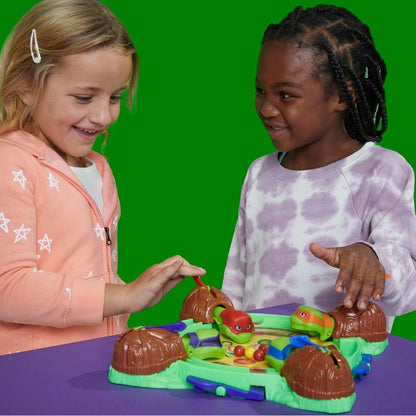 Two smiling girls playing a TMNT board game with turtle figures and colored balls