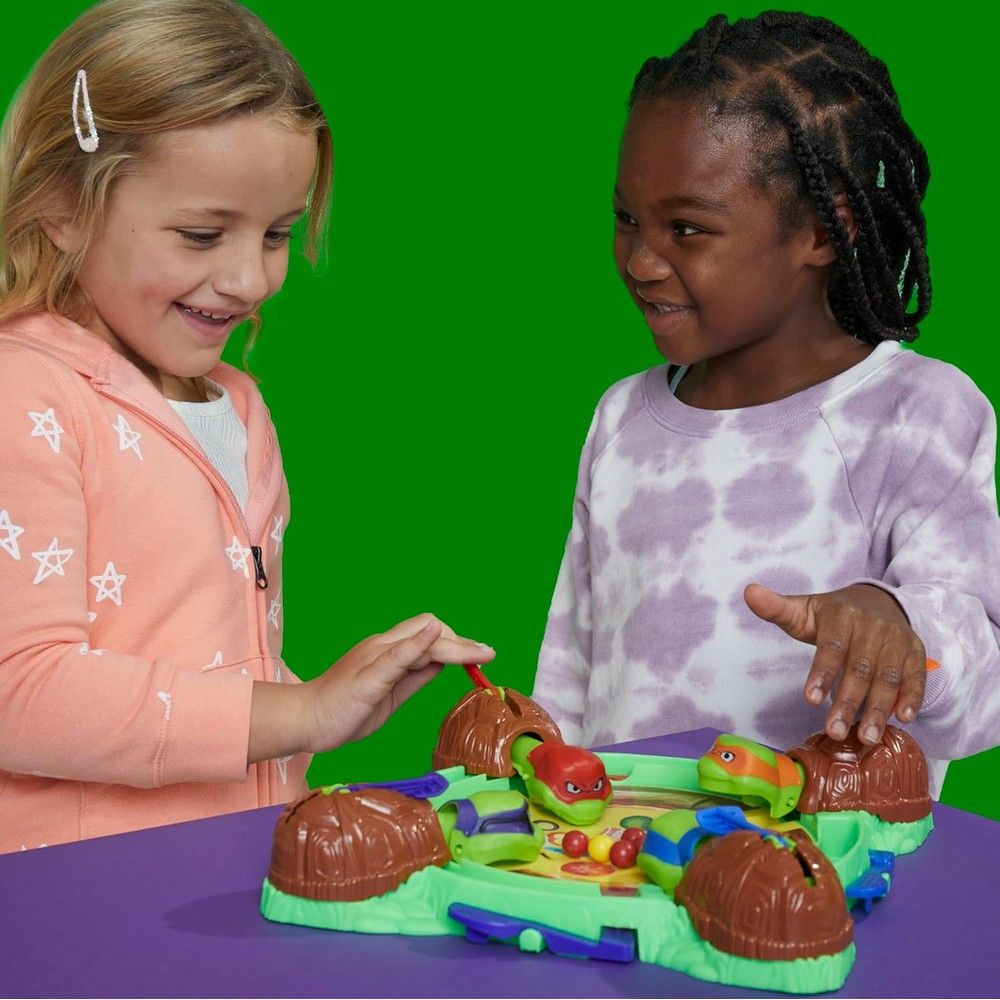 Two smiling girls playing a TMNT board game with turtle figures and colored balls
