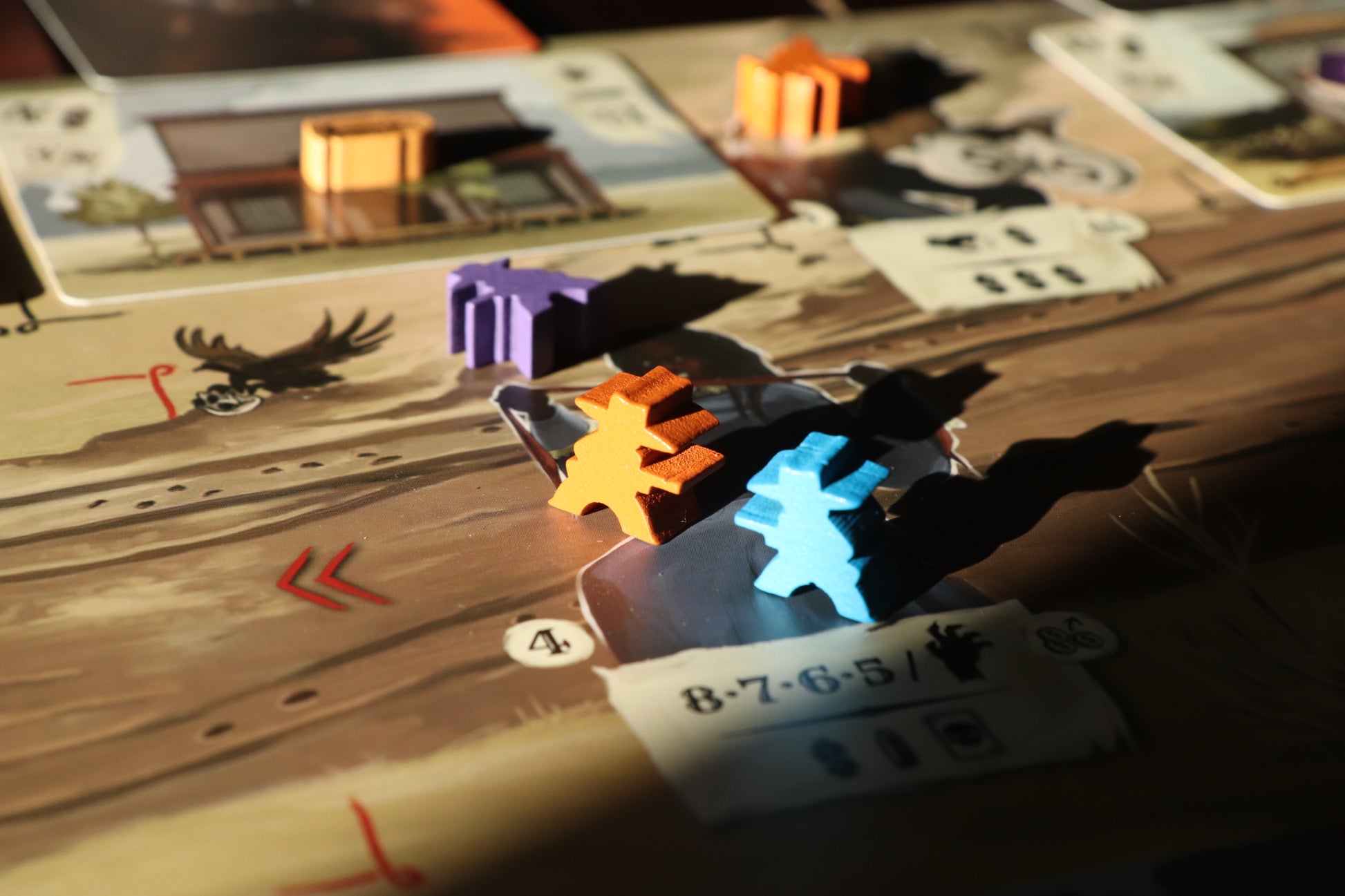 Orange, blue, and purple wooden meeples on a board game track, casting shadows in sunlight