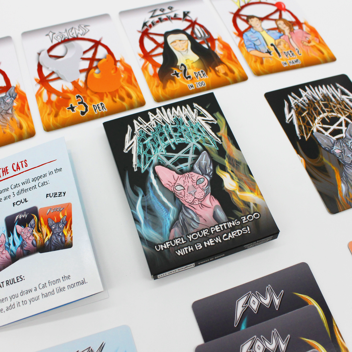 Satanicats game box and cards are displayed, the box shows a pink sphinx cat, while cards depict characters, pentagrams, and flames