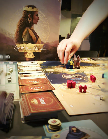 Hands play the strategy board game Sammur-ramat with detailed map cards and wooden pieces